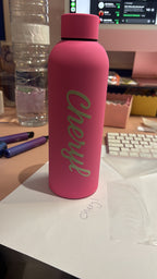 Pink sports insulated water bottle with 'Cheryl' branding in a casual indoor setting