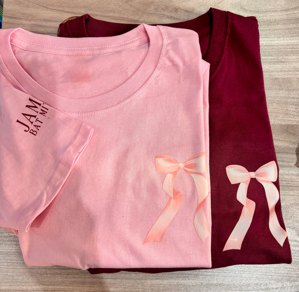 Folded pink and maroon event t-shirts with bow designs on a wooden surface