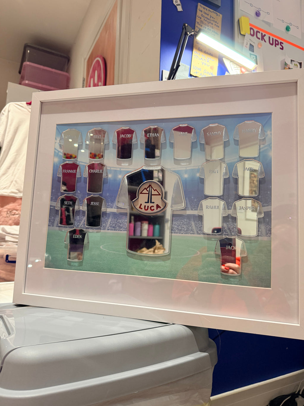 Framed football gift with various small acrylic shirts with engraved names on a blue background