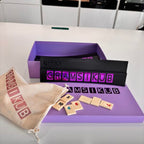 Gramsikub game set with purple box, wooden tiles, and drawstring bag on a white surface.