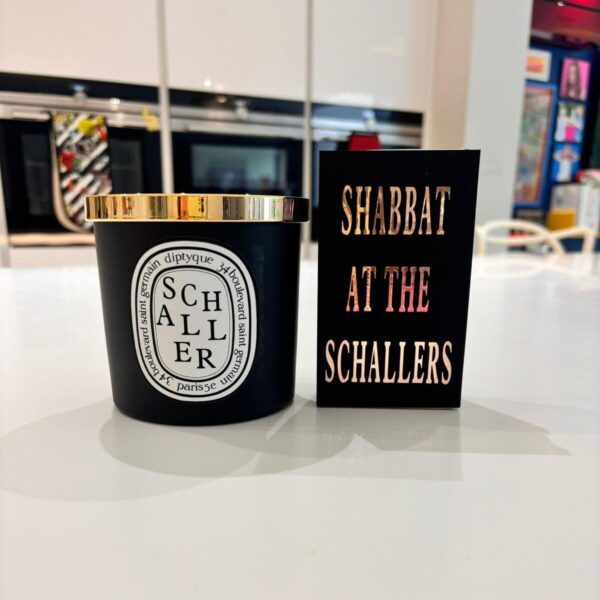 Gift set of a black Schaller candle with gold lid on a white surface, next to a black match box sleeve with 'Shabbat at the Schallers' text.