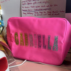 Pink washbag with 'GABRIELLA' in glittery letters on a desk with papers in the background