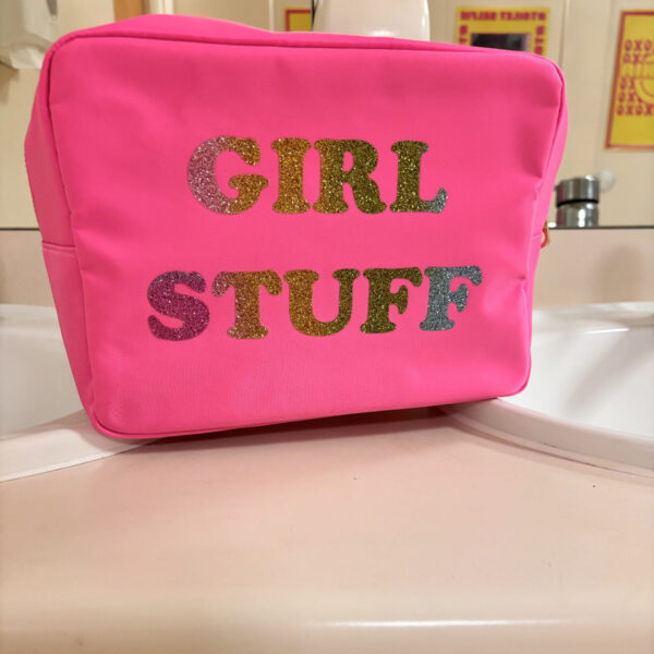 Pink washbag with 'GIRL STUFF' text in multicolour on a white surface.