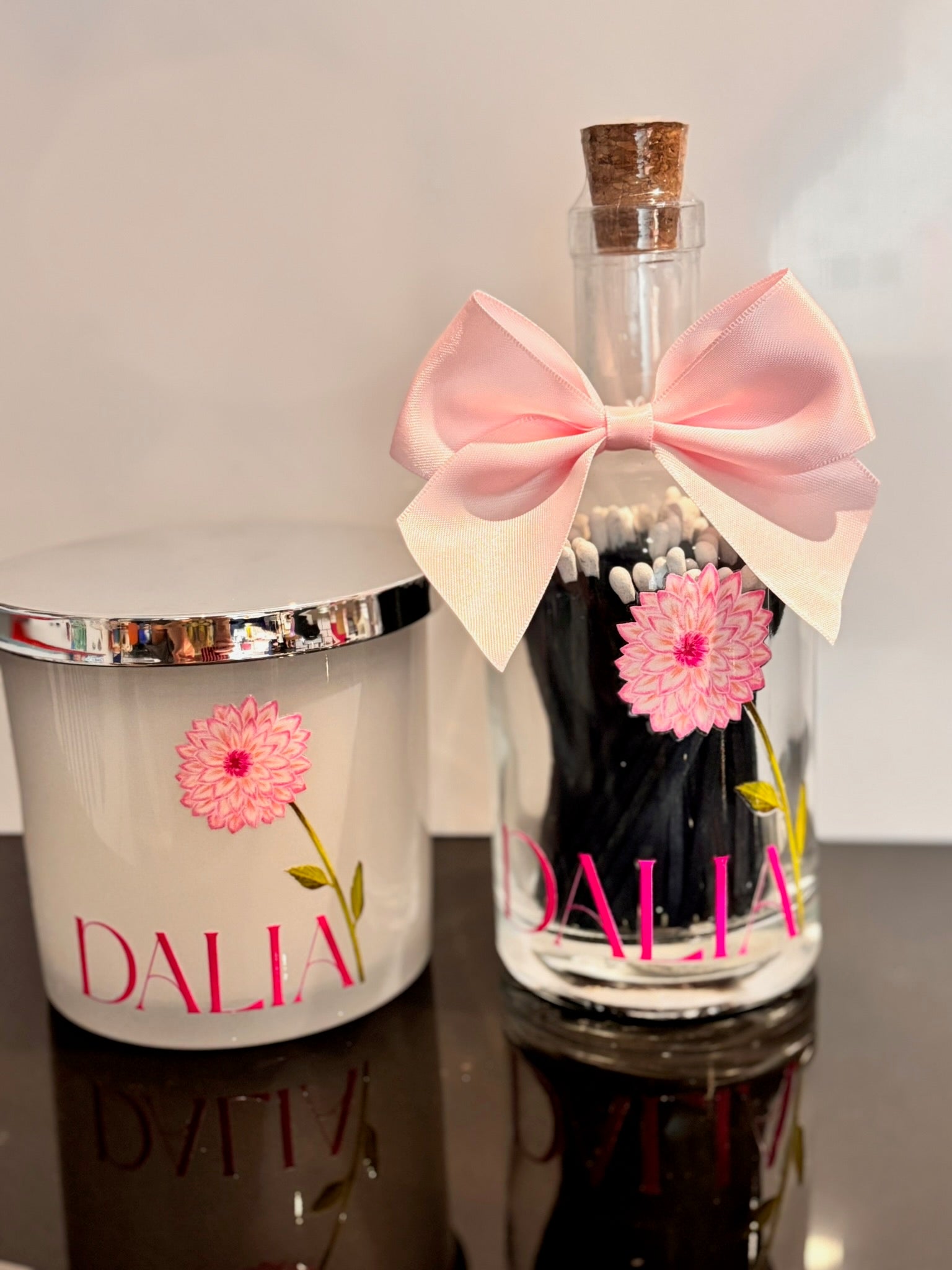 Glass bottle matches with pink bow and hairpins, next to a white container with pink flower design and 'Dalia' branding.