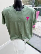 Green event t-shirt with a pink heart design on a drying rack outdoors.