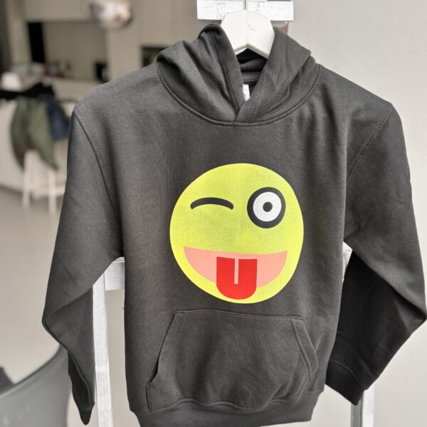 Grey hoodie with a yellow emoji face design on a hanger.