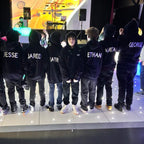 Group of people wearing black hoodies with names printed on the back, standing on a stage.