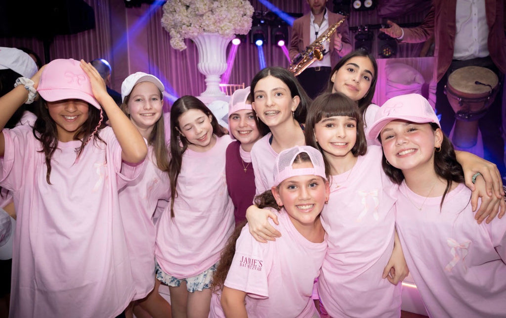Group of young girls in pink event t-shirts posing together in a festive setting with purple lighting.