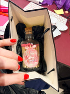 Hand holding a small match bottle with a pink label inside an open box on a desk.