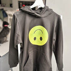 Grey hoodie with a yellow smiley face design on a hanger.