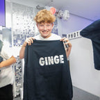 Person holding a black hoodie with 'GINGE' printed on it in an indoor setting.