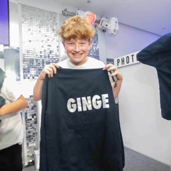 Person holding a black hoodie with 'GINGE' printed on it in an indoor setting.