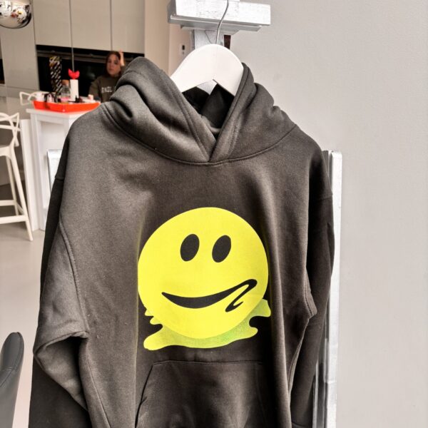 Grey hoodie with a yellow smiley face design on a hanger in a kitchen.