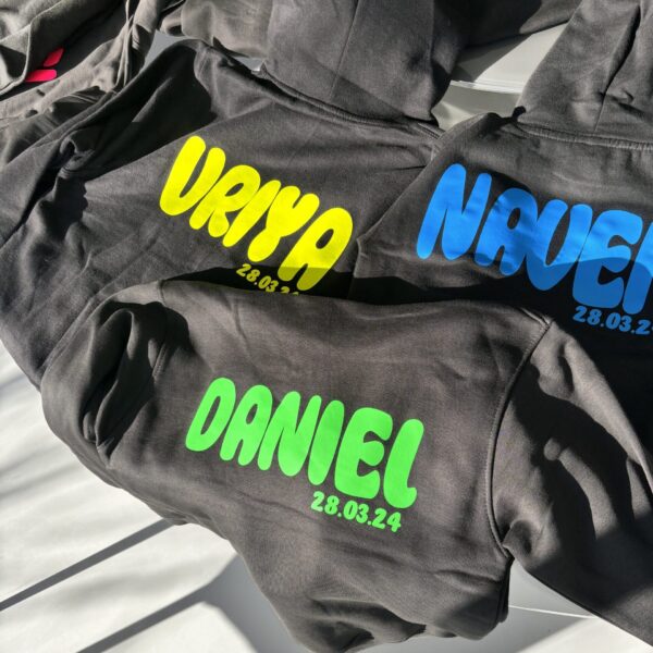 Black hoodies with personalised names and dates on a light background