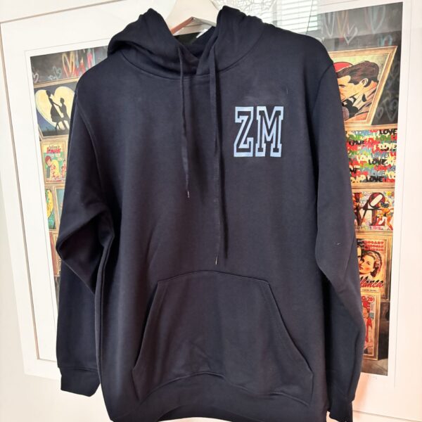 Black hoodie with 'ZM' logo on a hanger against a comic book-themed wall.
