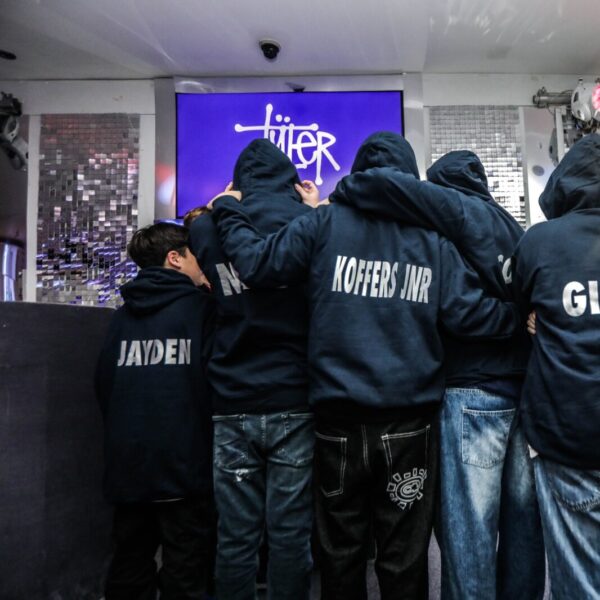 Group of people wearing hoodies with names on the back, gathered around a screen displaying a logo.