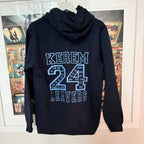 Black hoodie with 'KEREM 24 LEAVERS' text on the back, displayed against a wall with posters.