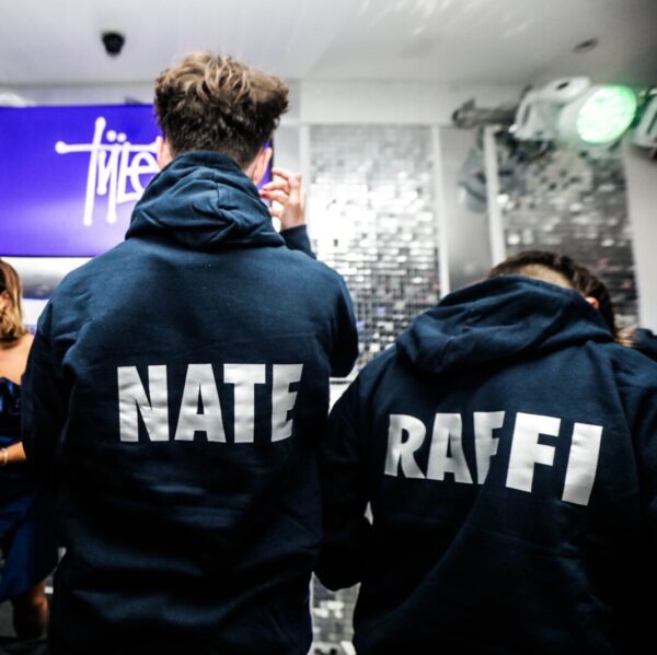 Two people wearing dark hoodies with 'NATE' and 'RAFFI' printed on the back, standing in a room with a disco ball.