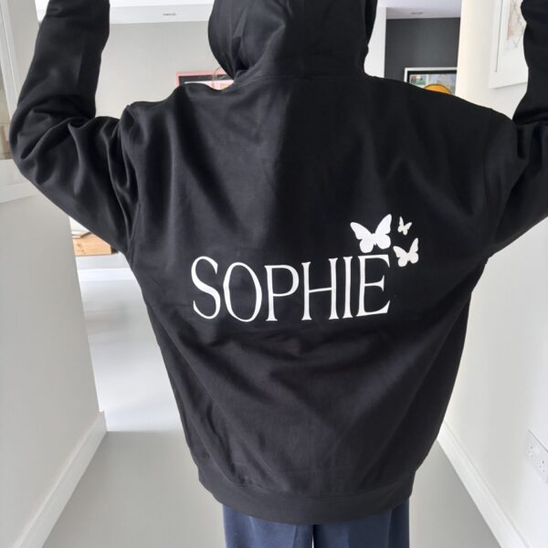 Black hoodie with 'SOPHIE' and butterfly designs on the back, worn by a person indoors.