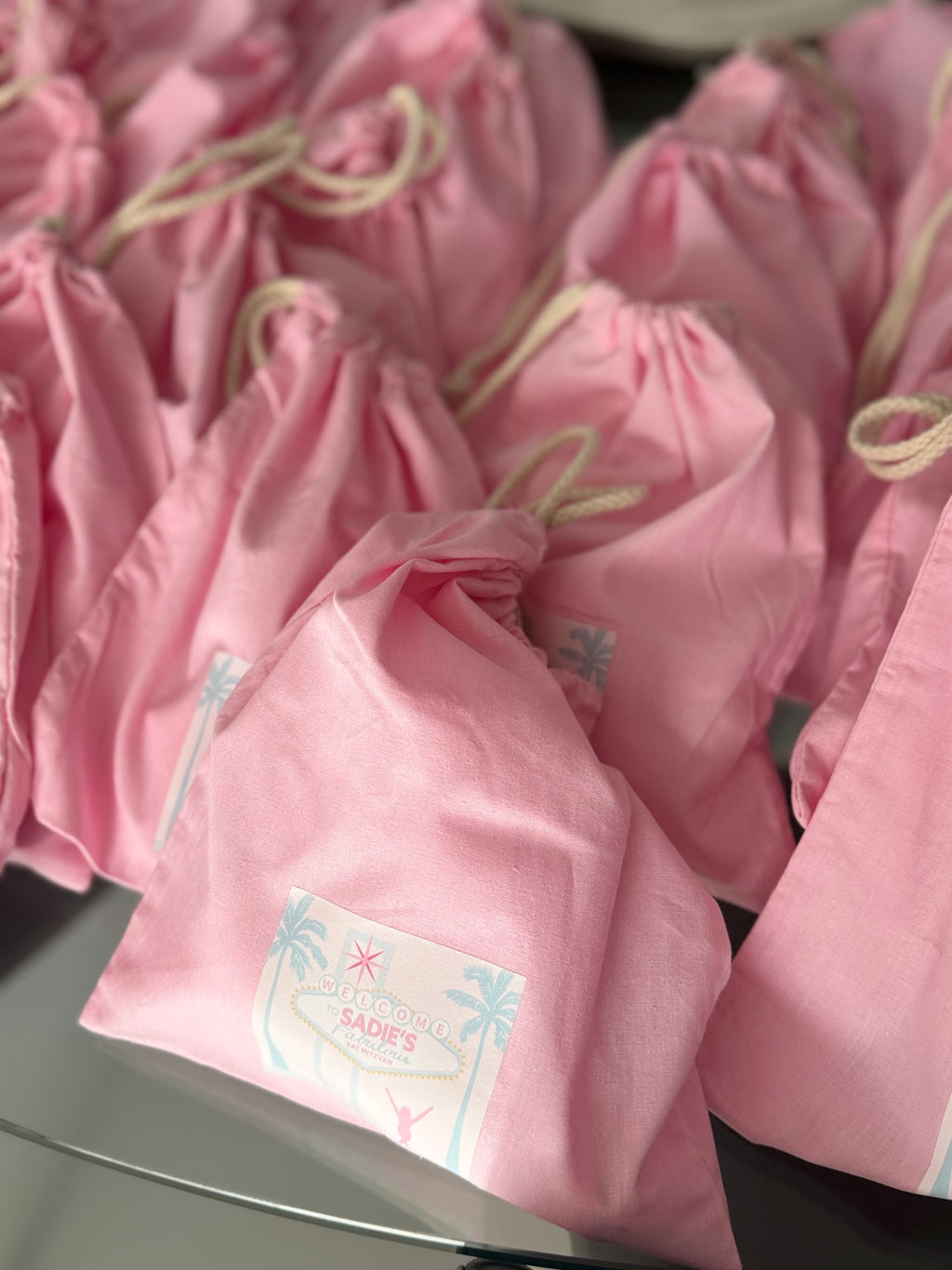 Pink drawstring personalised tote bags with labels on a reflective surface