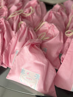 Pink drawstring personalised tote bags with labels on a reflective surface