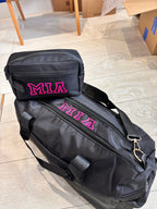 Black duffel bag and washbag with 'MIA' printed in pink on a tiled floor.