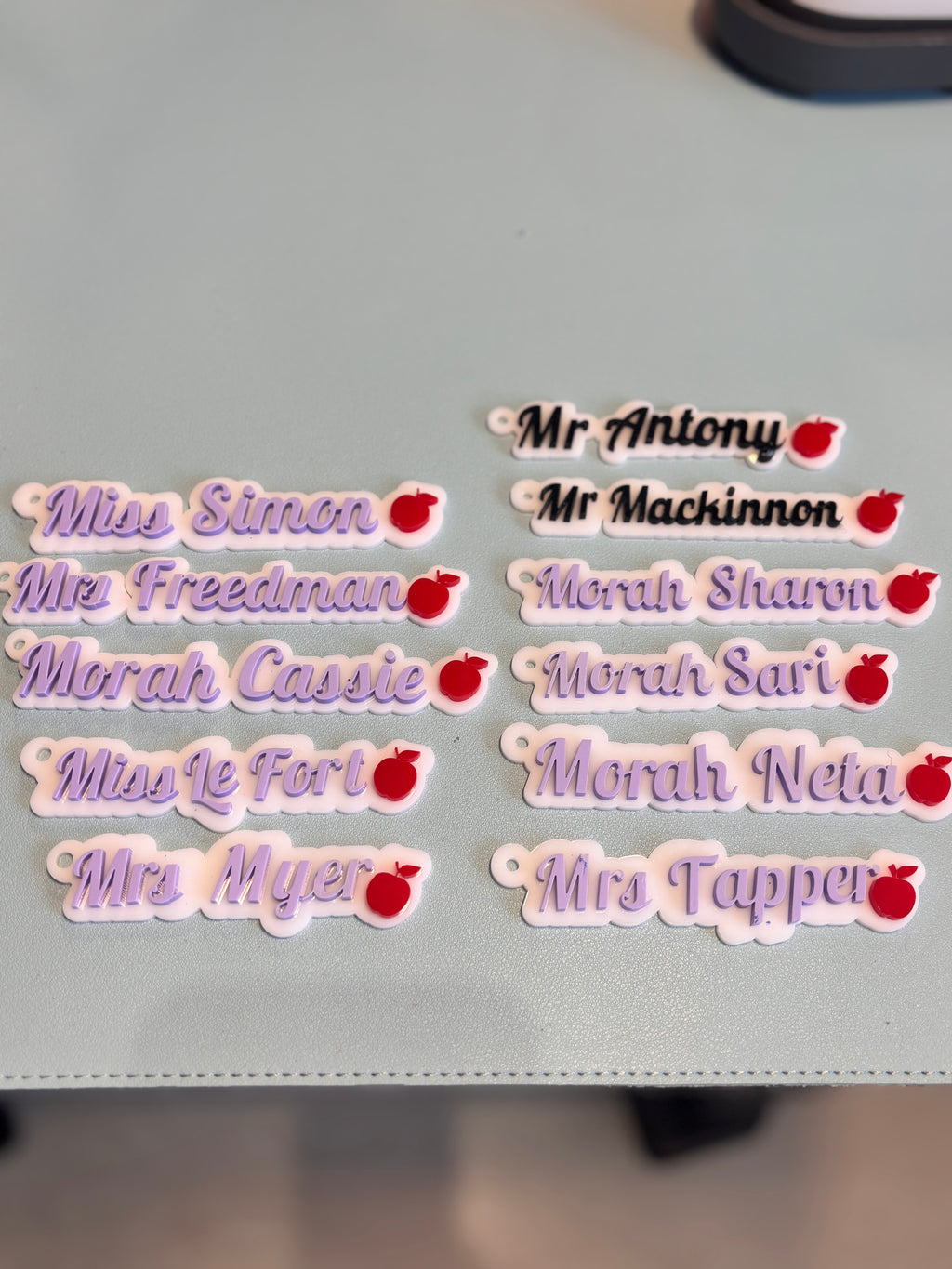 Keyrings with names and small red apple design on a grey surface