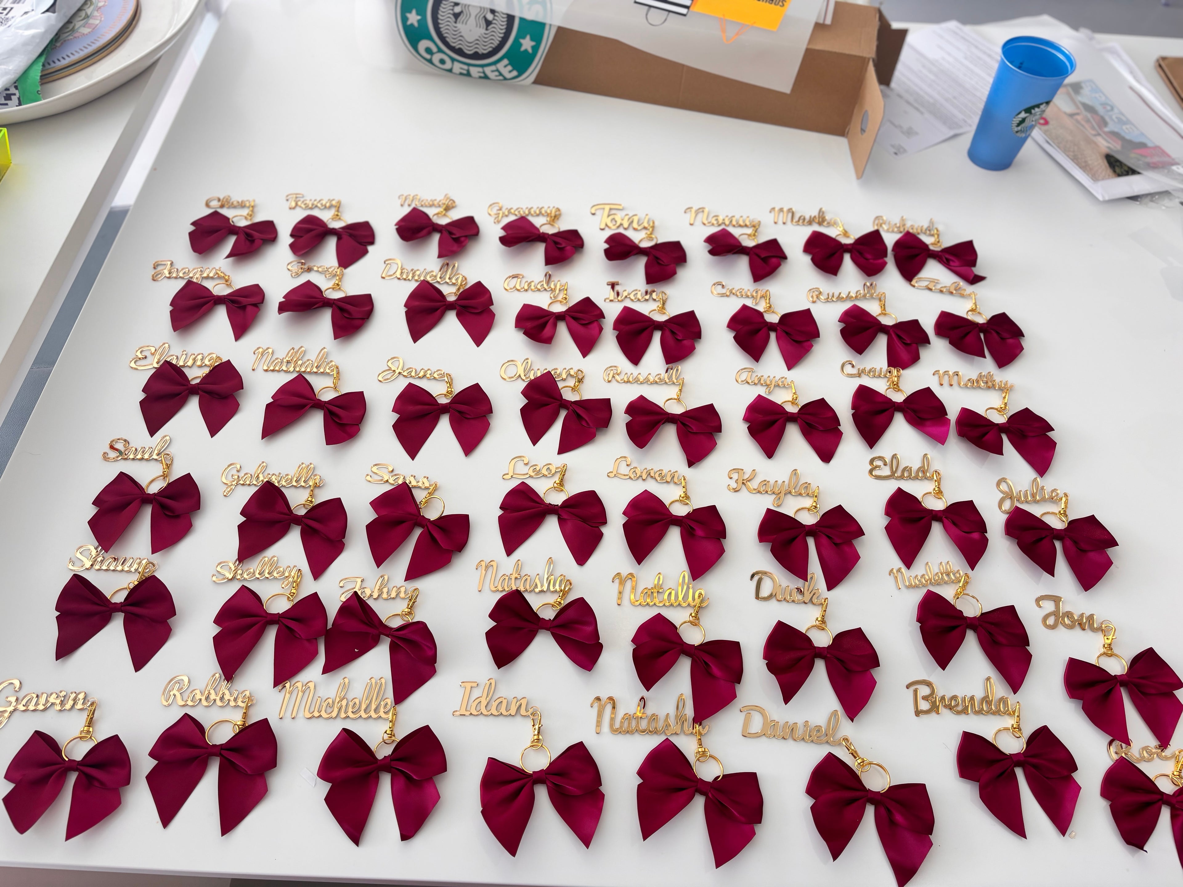Maroon bow keyrings with names on a white surface