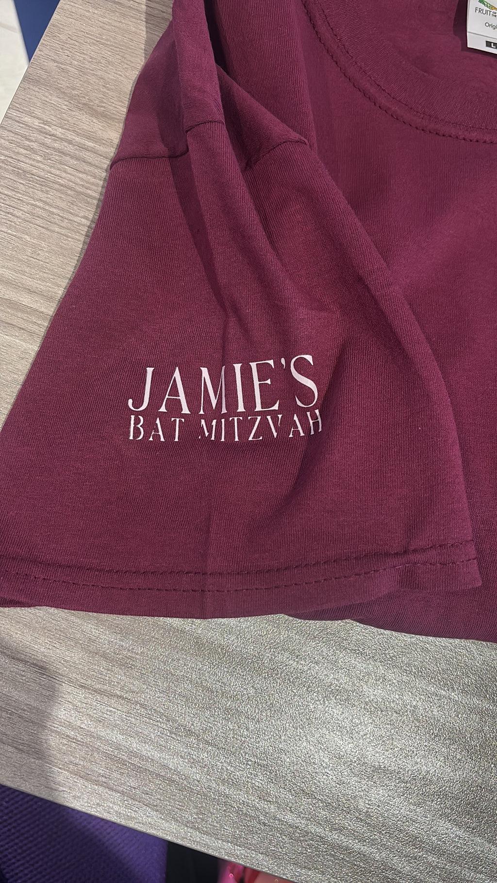 Maroon event t-shirt with 'JAMIE'S BAT MITZVAH' text on a textured surface