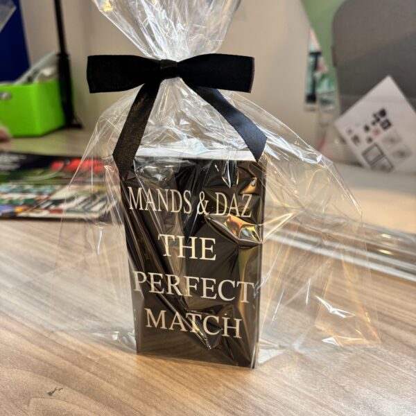 Black match box sleeve with 'Mands & Daz The Perfect Match' text, wrapped in clear cellophane with a black ribbon on a wooden surface.