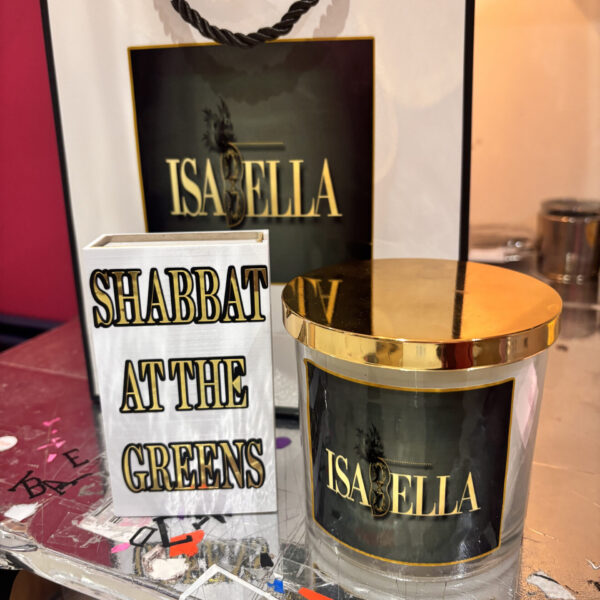 White match box sleeve with gold text 'Shabbat at the Greens' with a candle and branded bag saying 'Isabelle'.
