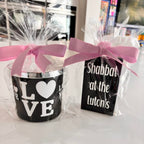 Two black match box sleeves with 'LOVE' and 'Shabbat at the Lutons' text, wrapped in cellophane with pink ribbons.