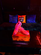 Neon pink high-top football boots on a black surface with colourful logo pillows in the background