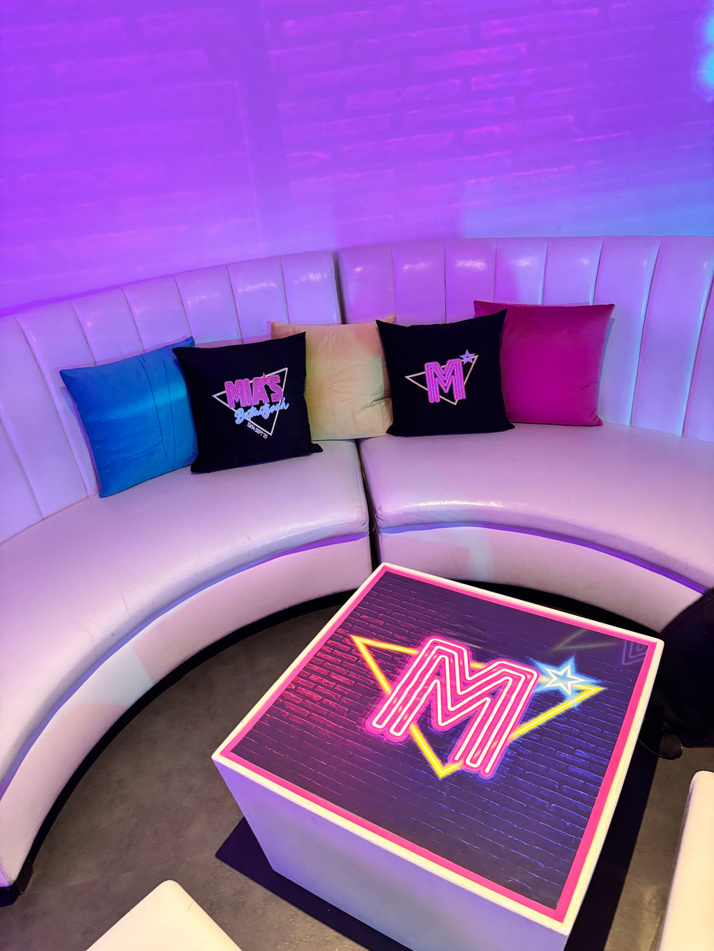 Neon table top sign with a logo with personalised logo pillows in the background