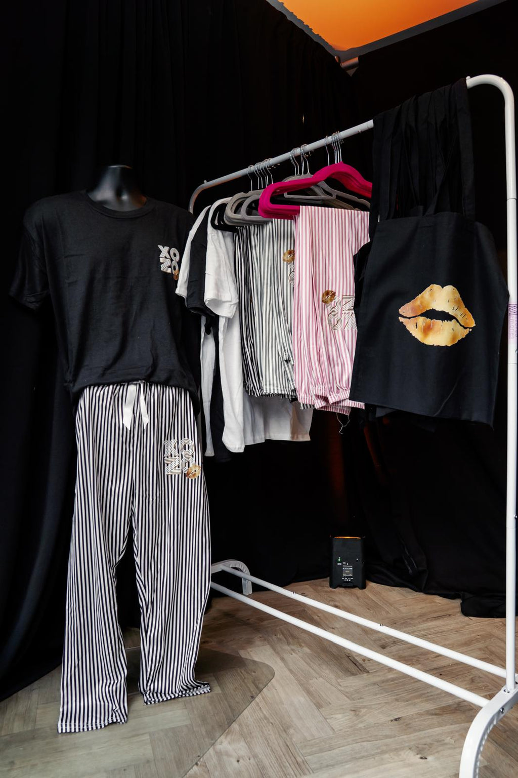 Clothing rack with various pyjamas such as shirts and pants on a wooden floor against a black wall.