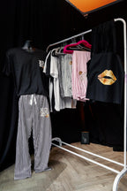 Clothing rack with various pyjamas such as shirts and pants on a wooden floor against a black wall.