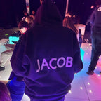 Person wearing a hoodie with 'JACOB' printed on the back in a social setting.