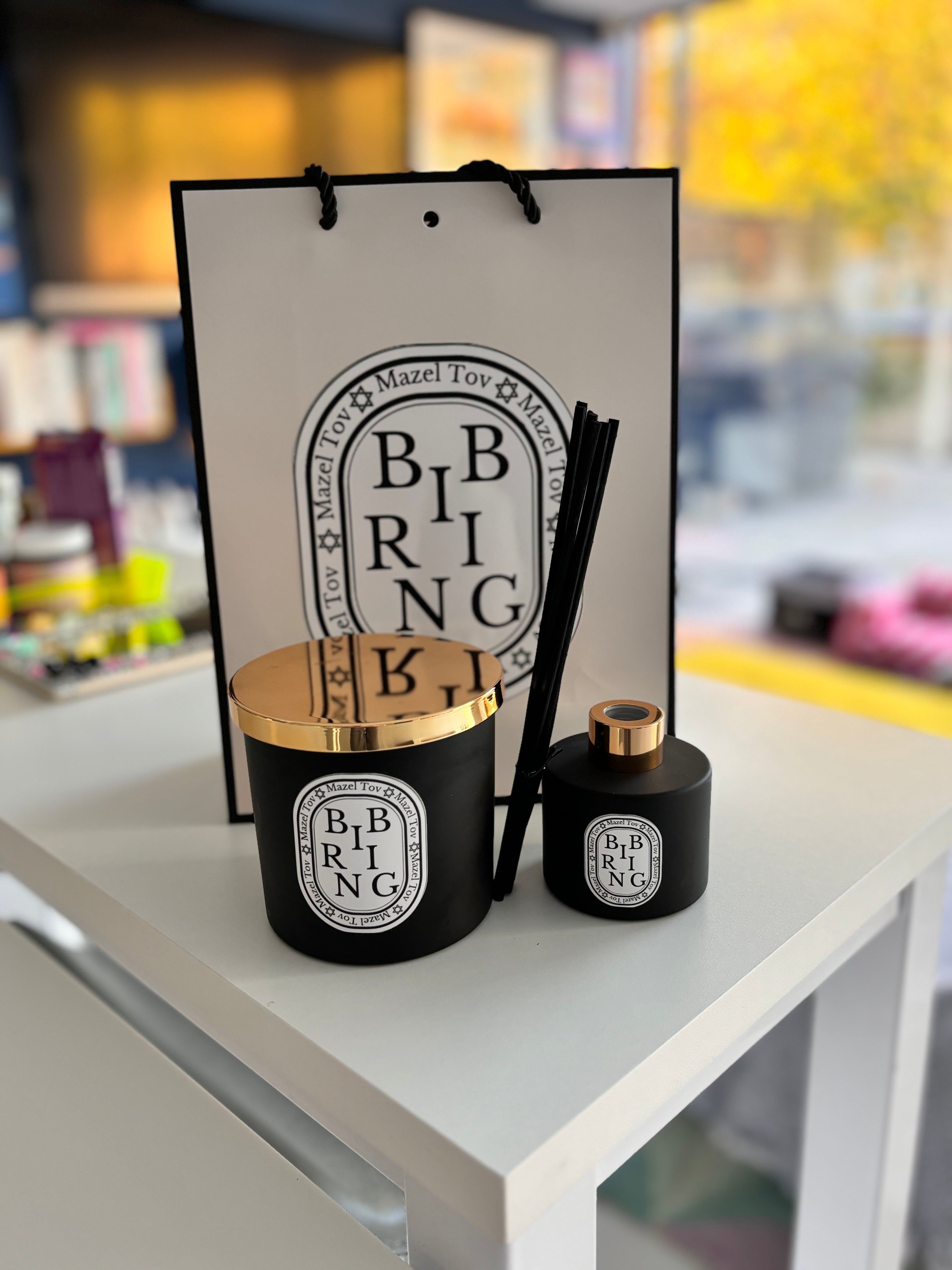Personalised 'Bibring' candle and diffuser set with gold lids on a white surface, with a branded bag in the background.