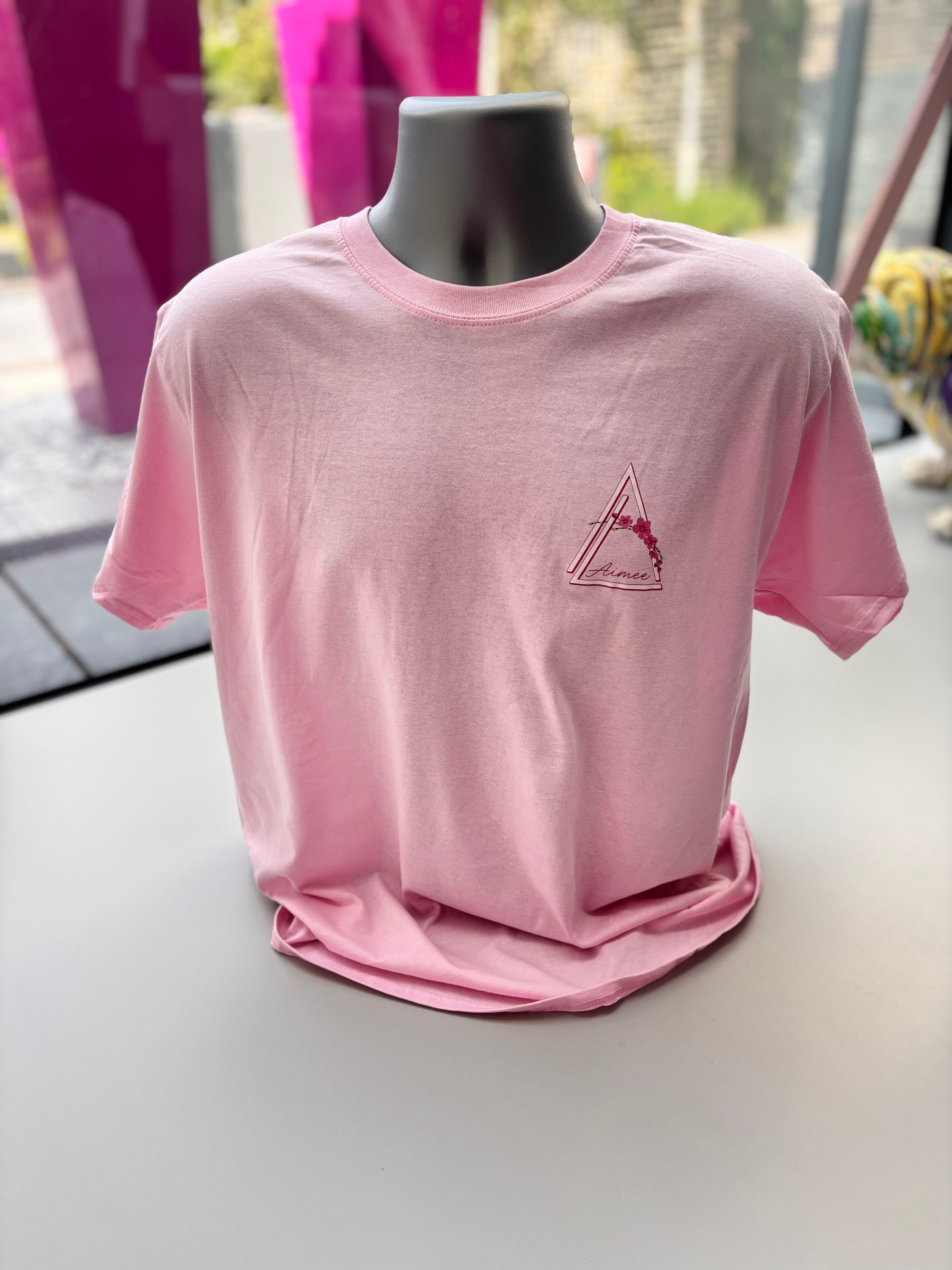 Pink event t-shirt with a logo on a mannequin against a blurred outdoor background