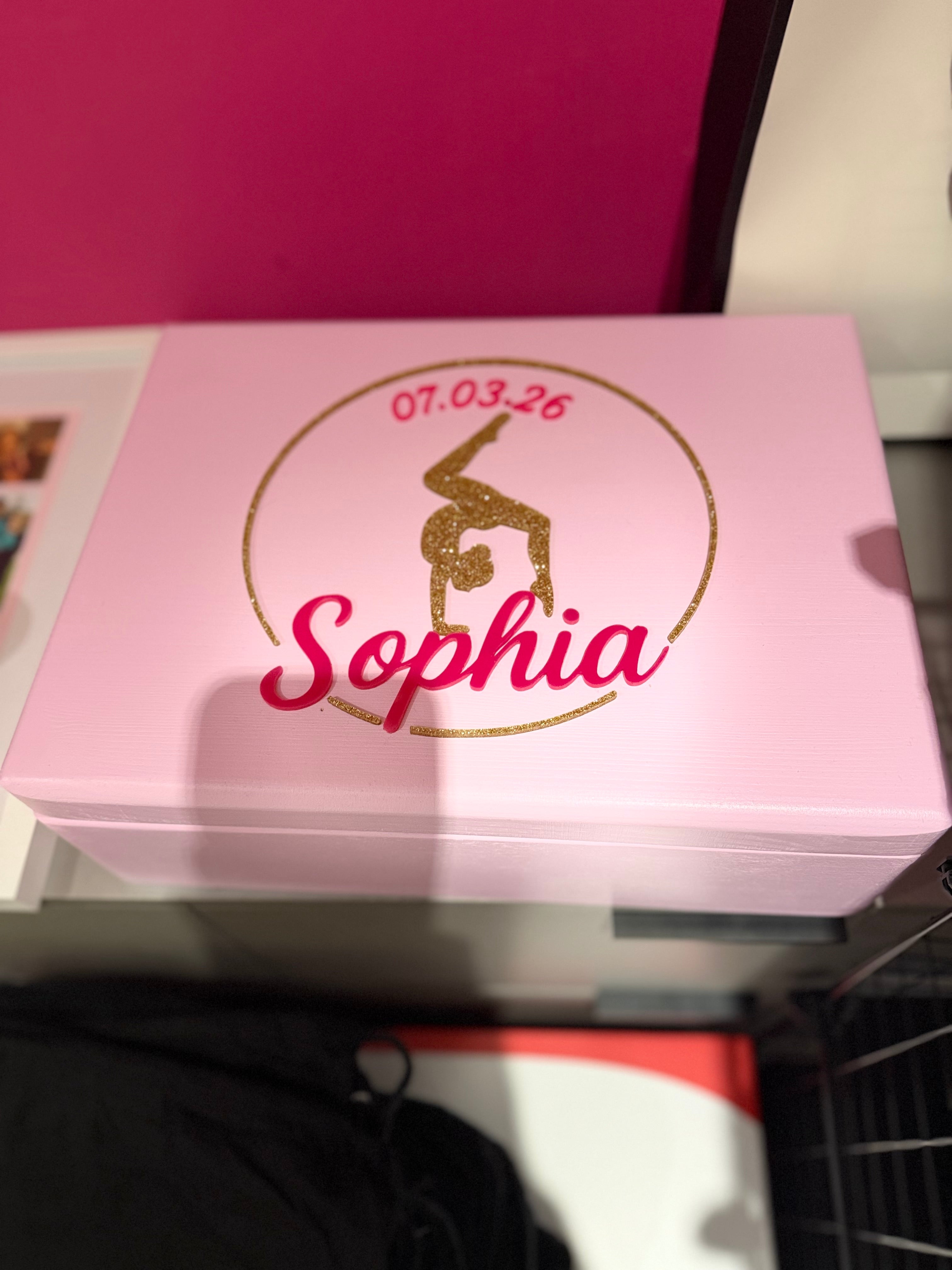 Pink keepsake box with 'Sophia' and a date printed on it, sitting on a surface.
