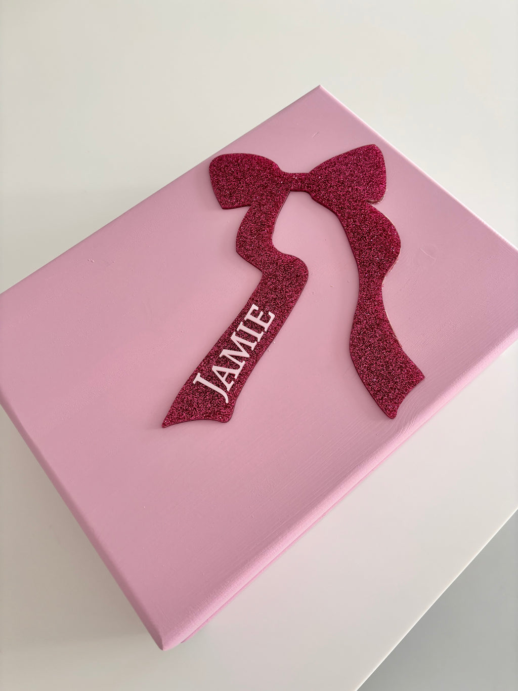 Pink keepsake box with a red glittery bow and 'JAME' text on a light grey background