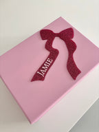 Pink keepsake box with a red glittery bow and 'JAME' text on a light grey background