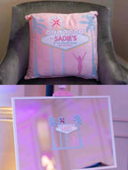 Pink personalised pillow with 'Welcome to Sadie's Fabulous' design on a chair, with a close-up inset showing the same design.