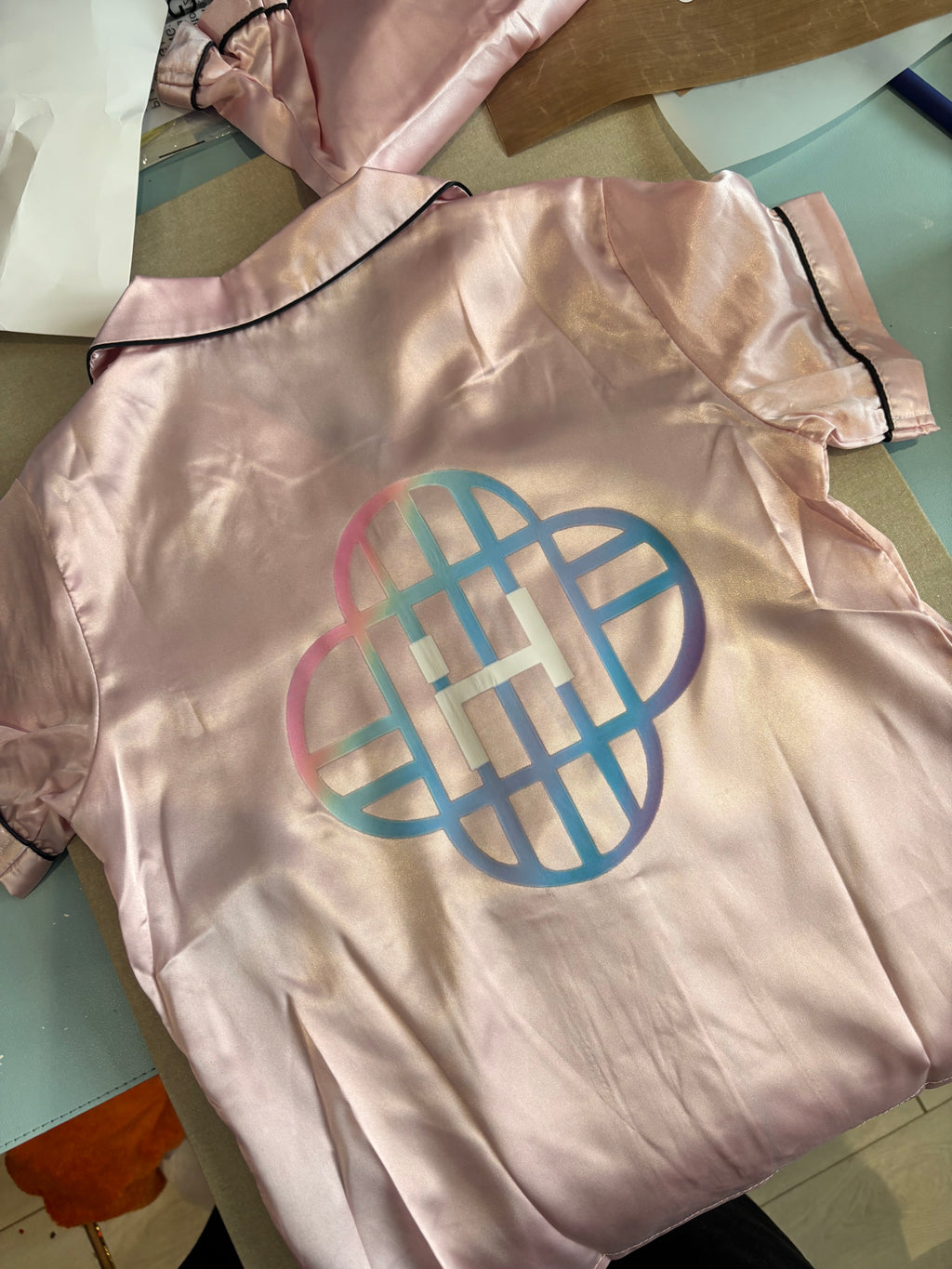 Pink satin pyjama top with a logo on a light-coloured surface