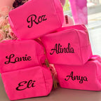 Pink washbags with names embroidered on them, surrounded by flowers.