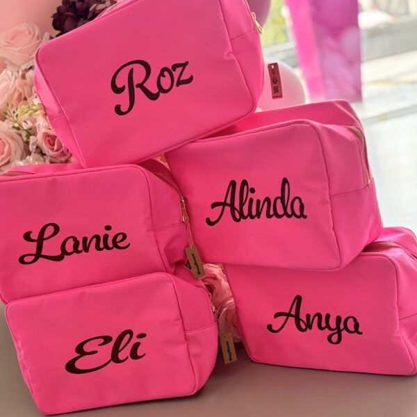 Pink washbags with names embroidered on them, surrounded by flowers.