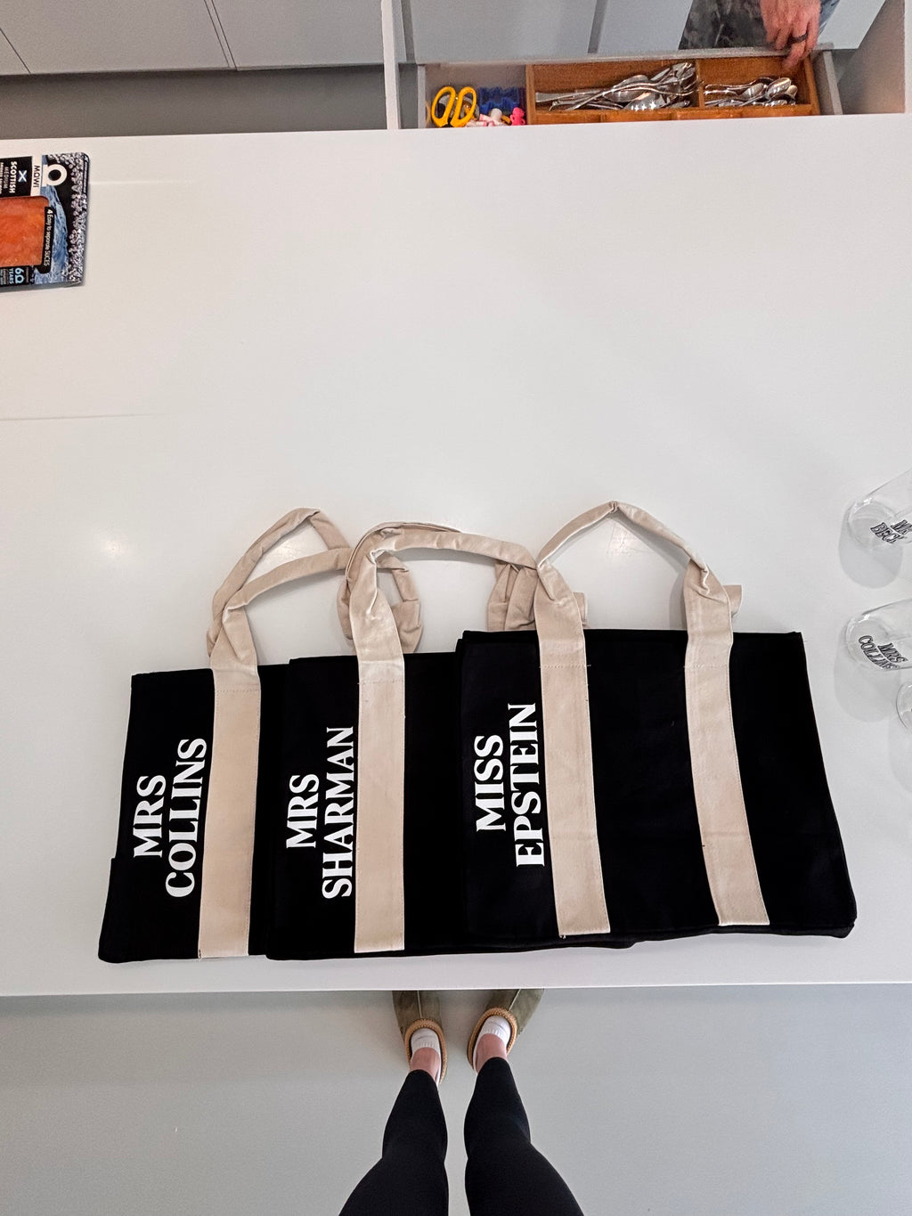 Set of black personalised tote bags with white text on a white surface