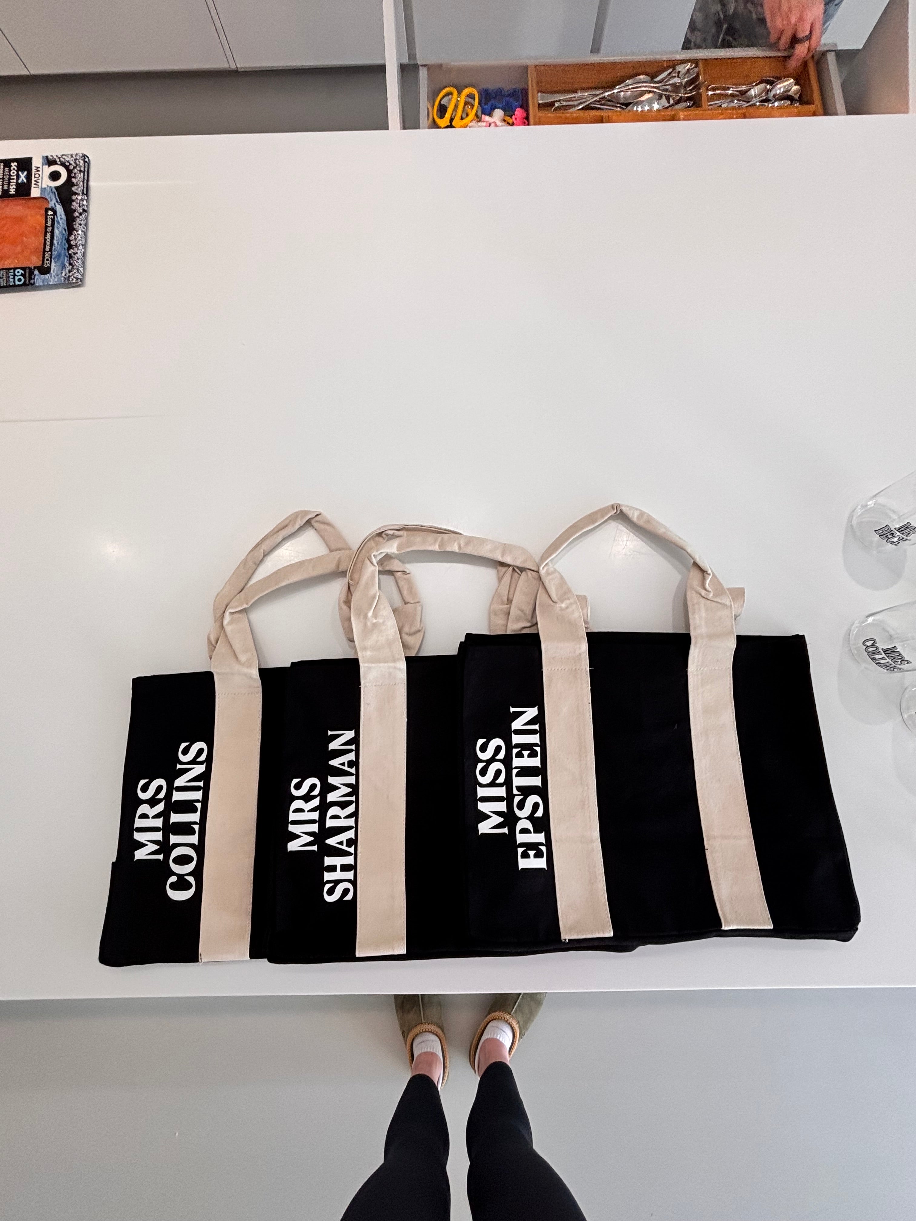 Set of black personalised tote bags with white text on a white surface