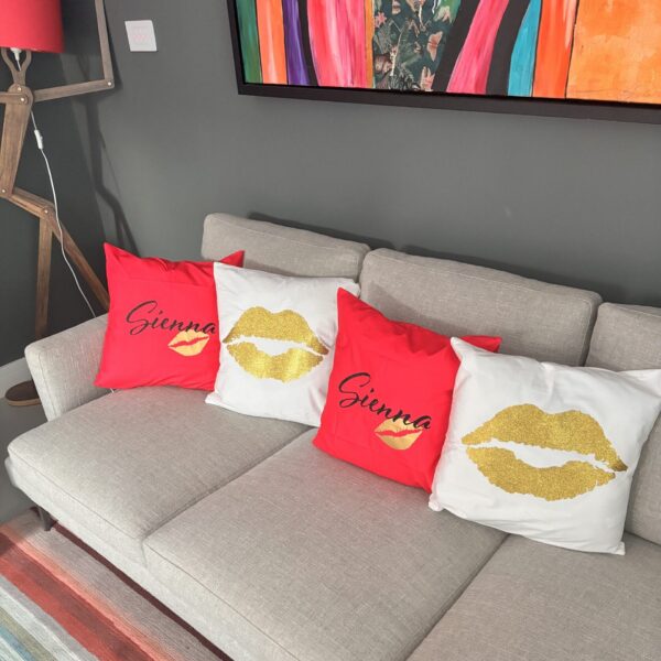 Grey sofa with decorative personalised silk pillow cases featuring names and gold lip prints in a living room setting.