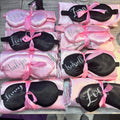 Set of personalised pink and white sleep masks with names printed on them, displayed on a table.